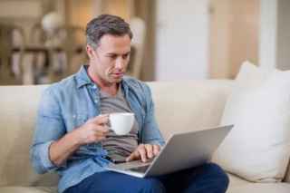 man drinking coffee while using laptop