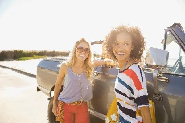 two women smiling next to car